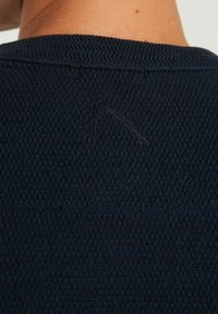 Marineblauer Strickpullover mit einem strukturierten Muster, das ein kleines, dezentes Detail am Halsauschnitt aufweist. Weiches, lässiges Design.