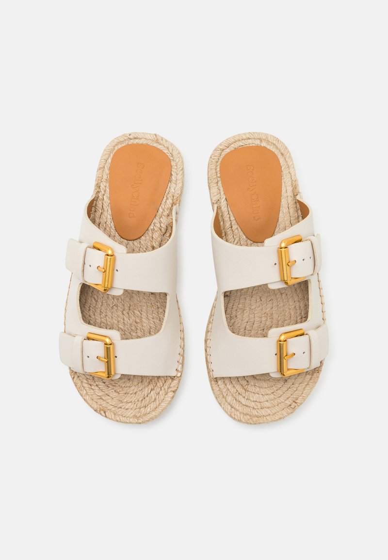 Weiße Ledersandalen mit zwei goldenen Schnallen, geflochtenen Jutesohlen und glatten braunen Fußbetten. Geschlossene Zehenpartie und offener Rücken.