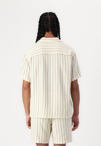Camicia a maniche corte a strisce crema e pantaloni abbinati, realizzati in tessuto testurizzato con leggere linee verdi, caratterizzati da una vestibilità rilassata e colletto.