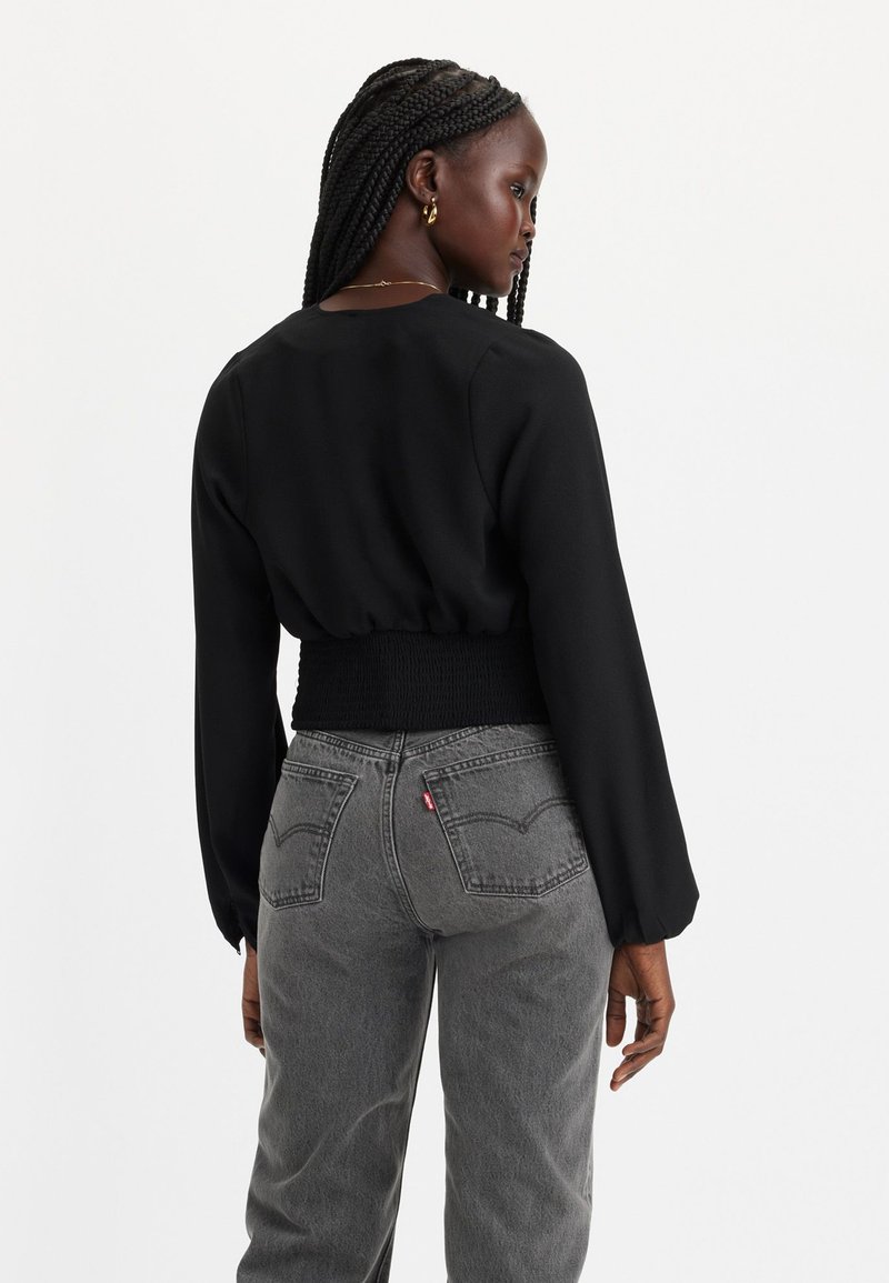 Schwarze Bluse mit langen, gepufften Ärmeln und gerafftem Taillenbund, kombiniert mit hochgeschnittenen grauen Jeans mit Gesäßtaschen und Logoetikett.