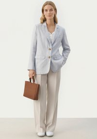 Světlomodrý lněný blazer s dvěma knoflíky, v kombinaci s béžovými kalhotami širokého střihu. Modelka drží malou hnědou koženou tašku. Bílé boty dotvářejí vzhled.