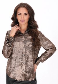 Metallinhohtoinen pronssinvärinen nappipaita, jossa on teksturoitu pinta, pitkät hihat ja kiiltävät napit, yhdistettynä mustiin alaosaan.