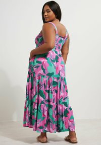 Maxime dress in lightweight fabric with a vibrant floral pattern featuring pink, green, and teal. It has a smocked bodice, adjustable straps, and a tiered hem.