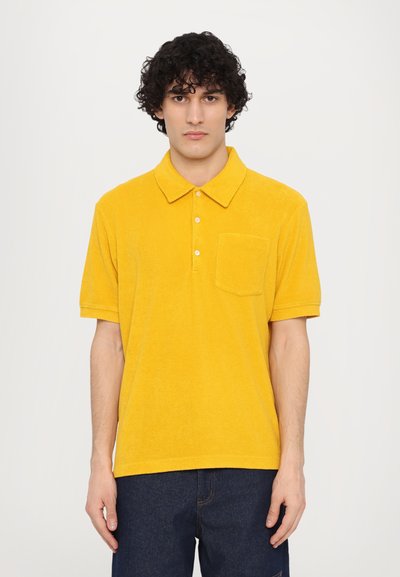 Polo shirt din terry galben, cu guler, placket cu trei butoane și un singur buzunar pe piept. Mâneci scurte, textură moale și croială lejeră.