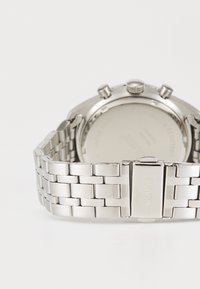 Ασημένιο μεταλλικό βραχιόλι ρολογιού με κούμπωμα που είναι χαραγμένο με το "CLUSE" και η πίσω πλευρά της στρογγυλής θήκης του ρολογιού έχει τρία κουμπιά ελέγχου.