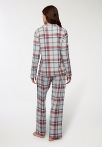 Set di pigiama a scacchi composto da una maglietta a maniche lunghe e pantaloni larghi grigi, rossi e blu, con colletto a bottone e texture di tessuto morbida.