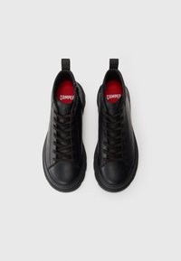 Black leather sneakers with round toe, thick sole, brown laces, and red insoles featuring branding. Smooth texture and minimal design.
