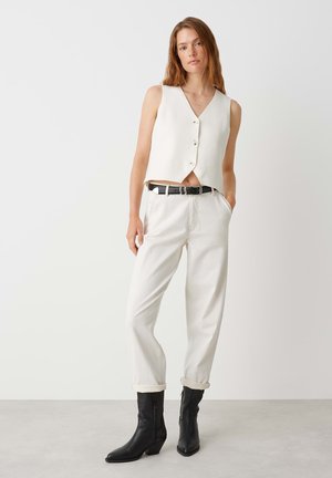 White cropped vest with button closure, paired with loose white trousers and black heeled boots. Simple design with a clean color palette.