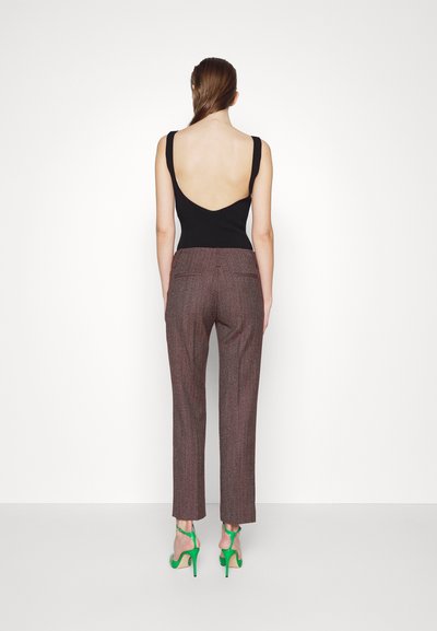 Μαύρο αμάνικο τοπ με χαμηλή πλάτη σε V, συνδυασμένο με υφασμάτινα παντελόνια ψηλόμεσɩα σε καφέ καρό σχέδιο και πράσινα ψηλοτάκουνα σανδάλια.