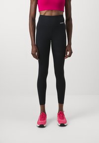 Melnas augstās leggingas ar perforētiem akcentiem, apvienotas ar spilgti rozā krāsas kroptopu un rozā sporta apaviem. Gluda, elastīga auduma struktūra.