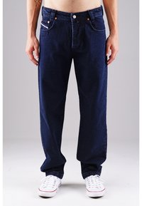 Marineblaue Denim-Jeans mit geradem Schnitt, fünf Taschen und dezenten orangenen Nähten. Kombiniert mit weißen Sneakern mit niedrigem Schaft.