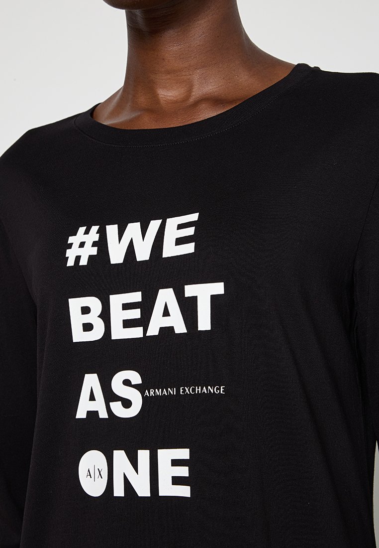 Maglietta nera a maniche lunghe con testo bianco audace "#NOI VINCIAMO COME UNO" e logo "ARMANI EXCHANGE", realizzata in morbido cotone.