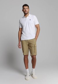 Witte poloshirt met een klein zwart embleem, khaki cargo shorts met zijzakken en witte sneakers met marineblauwe accenten. Glad katoen gevoel.