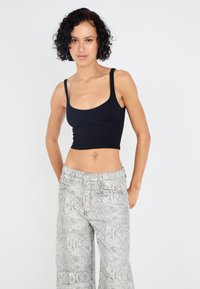 Zwarte geribbelde crop top met dikke bandjes, gecombineerd met wijde broek met een slangenprint in grijs en wit.