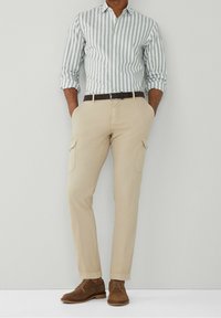 Skjorte med knappelukning i lysegrønne og hvide striber, kombineret med beige cargobukser med sidelommer og brune ruskindssko.