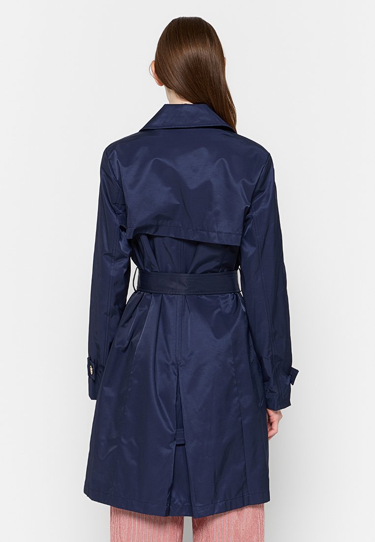 Cappotto trench navy con finitura lucida, vita con cintura e design doppiopetto. Presenta un ampio colletto e una fessura sulla schiena per facilitare i movimenti.