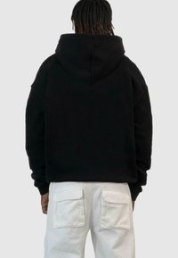 Juodas per didelis gobtuvu megztinis, pasižymintis minkšta tekstūra. Dėvimi su baltais cargo kelnėmis, turinčiomis dideles kišenes.