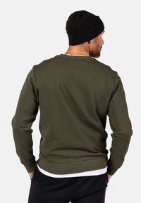 Felpa verde scuro con scollatura rotonda e polsini a coste, abbinata a un berretto nero. Tessuto dalla consistenza liscia, design casual.