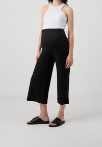 Svarta ribbade culotter med en flexibel midja, i kombination med en vit åtsittande linne och svarta slip-on sandaler. Enkelt och avslappnat design.