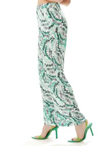 Wide-leg pants feature a white base with green and black fern-like patterns. Paired with green high-heeled sandals and a smooth texture.
