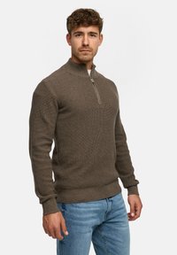 Brun lynlåstruet sweater med ribbet tekstur, lange ærmer og en tætsiddende design, parret med lyseblå denim jeans.