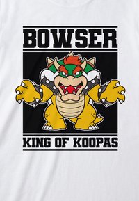 Bílá tričko s barevným grafickým motivem Bowsera, kreslené postavy, s černým textem "BOWSER" a "KRÁL KOUPA" nahoře a dole.