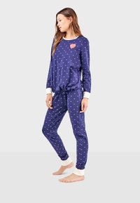 Ensemble de pyjama marine en tissu doux, avec un graphique en forme de cœur, des accents blancs aux poignets et de petits motifs en cœur sur l'ensemble. Pantalon avec une taille élastique.