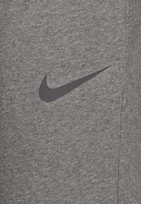 Grauer sportlicher Stoff mit einer glatten Textur, der ein großes schwarzes Nike-Swoosh-Logo trägt. Das Material scheint dehnbar und atmungsaktiv zu sein.