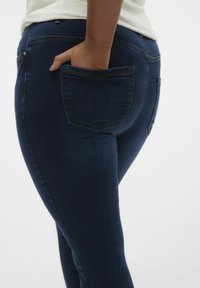 Jeans de denim azul oscuro con corte slim, que cuentan con un bolsillo trasero y costuras en contraste. El material es suave y tiene un ligero estiramiento.