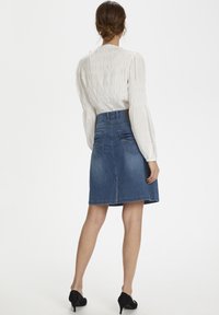 Denimkjol med figurnära midja, utsvängd nederdel och bakfickor. Bärs med en vit smockblus och svarta högklackade skor.