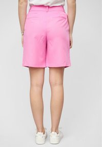 Shorts di cotone rosa con davanti piatto, tasche posteriori e taglio dritto, abbinati a sneakers bianche. Design semplice, lunghezza fino a metà coscia.
