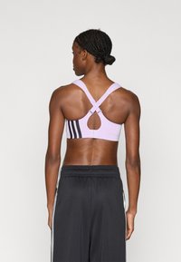 Ανοιχτό μωβ αθλητικό σουτιέν με σχέδιο σταυρωτής πλάτης. Διαθέτει άνοιγμα σε σχήμα κλειδιού και τρεις μαύρες ρίγες στο πλάι. Λεία υφή.