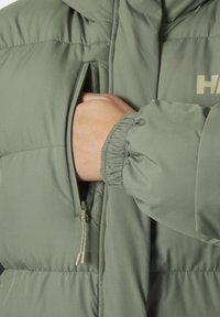 Chaqueta puffer verde con un bolsillo con cremallera. La tela tiene una textura suave, con puños elásticos y un diseño acolchado horizontal elegante.