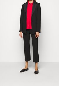 Blazer noir avec des revers en satin, associé à un chemisier rouge et un pantalon noir court, complété par des ballerines noires. Design simple et ajusté.