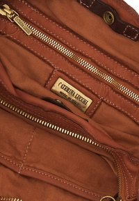 Interno di una borsa a mano in tessuto marrone con tasche con zip, una cerniera in tonalità oro e un'etichetta che recita "Caterina Lucchi Made in Italy."