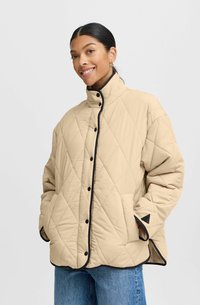 Veste matelassée beige avec un col montant, des finitions noires et des boutons-pression. Dotée de poches latérales et d'une texture en motif de losanges.