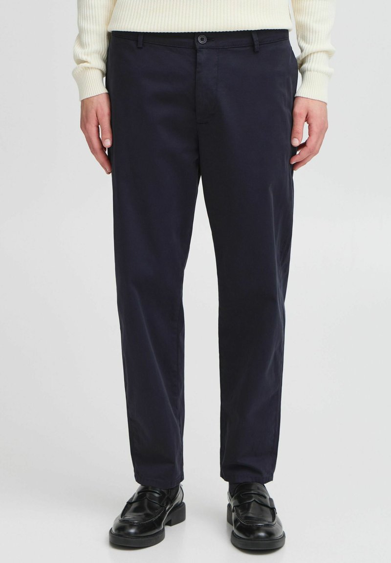 Navy blue trousers made of smooth fabric, featuring a button closure, slanted side pockets, and a tailored fit. Black shoes complete the look.