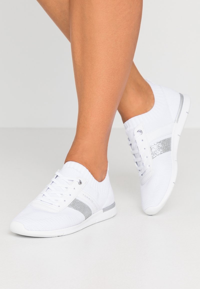 Vita stickade sneakers med silverglitterrand, snörning, rund tå, elastisk ankelskärp och texturerad sula.