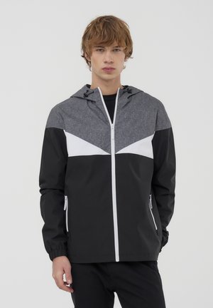 Giacca con cappuccio nera e grigia, caratterizzata da chiusura zip frontale, accenti bianchi in contrasto, polsini elastici e un materiale leggero e resistente all'acqua.