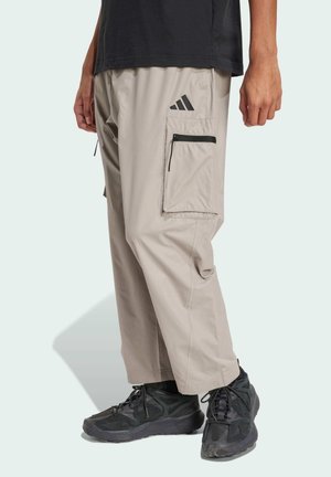 Pantalones cargo beige con bolsillos con cremallera, hechos de un tejido ligero. Presenta acentos negros, incluyendo un logo y una cremallera en contraste.