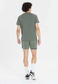 Sportoutfit voor heren bestaande uit een groene t-shirt met korte mouwen en bijpassende shorts. Het materiaal is soepel, met een comfortabele pasvorm en minimale ontwerpdetails.