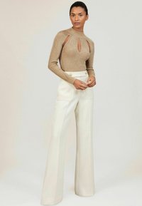 Auksinis megztinis su išpjovomis, aukštu kaklu ir ilgomis rankovėmis; derinamas su baltais plačiakojais kelnais, turinčiais aukštą juosmenį ir dvi kišenes.