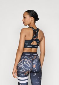 Top desportivo preto com padrões abstratos coloridos, apresentando um design com alças em corrida. Leggings de cintura alta com um design semelhante e detalhes listrados.