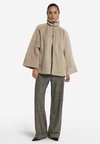 Beige fleecetröja med hög krage, dragkedja fram och nedfallna ärmar. Kombinerad med byxor i herringbone-mönster med vida ben och spetsiga skor.