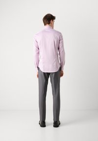Lila Langarmshirt mit abgerundetem Saum, kombiniert mit grauen Maßanzughosen und schwarzen Schuhen, von hinten betrachtet.