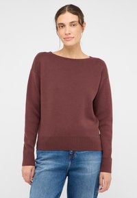 Burgunderfarbener Strickpullover mit einem Bootsausschnitt, gerippten Bündchen und Saum. Getragen über hellblauen Jeans.