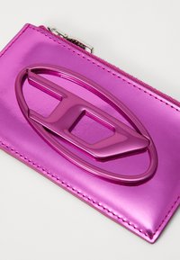 Pink metallic cardholder with a smooth texture, featuring an oval cutout design and a silver zipper.