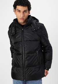 La chaqueta acolchada negra presenta un diseño acolchado, bolsillos con cremallera, capucha desmontable y puños elásticos. Fabricada con material sintético.