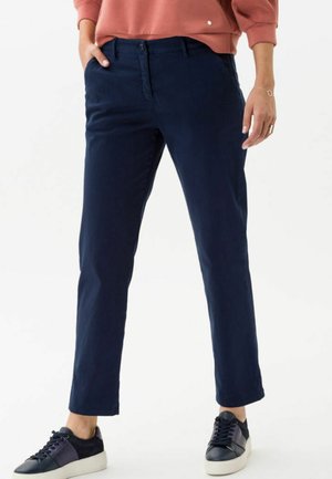 Pantalones de algodón azul marino con corte recto y bolsillos laterales, con cierre de botón y cremallera, usados con zapatillas azul marino y blancas.