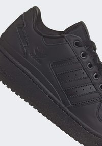 Svart lädersneaker med en texturerad sula, som har tre distinkta horisontella ränder, runda snörningar och subtil branding på sidan.